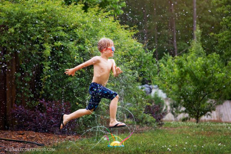 Atlanta lifestyle photographer, boy in summer running through a sprinkler with goggles on