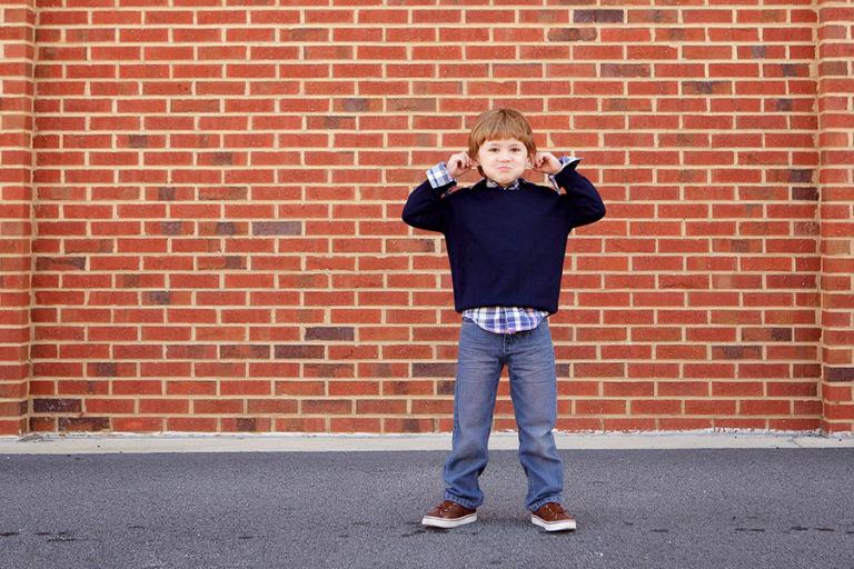 children's photographer Villa Rica, boy making a funny face by brick wall