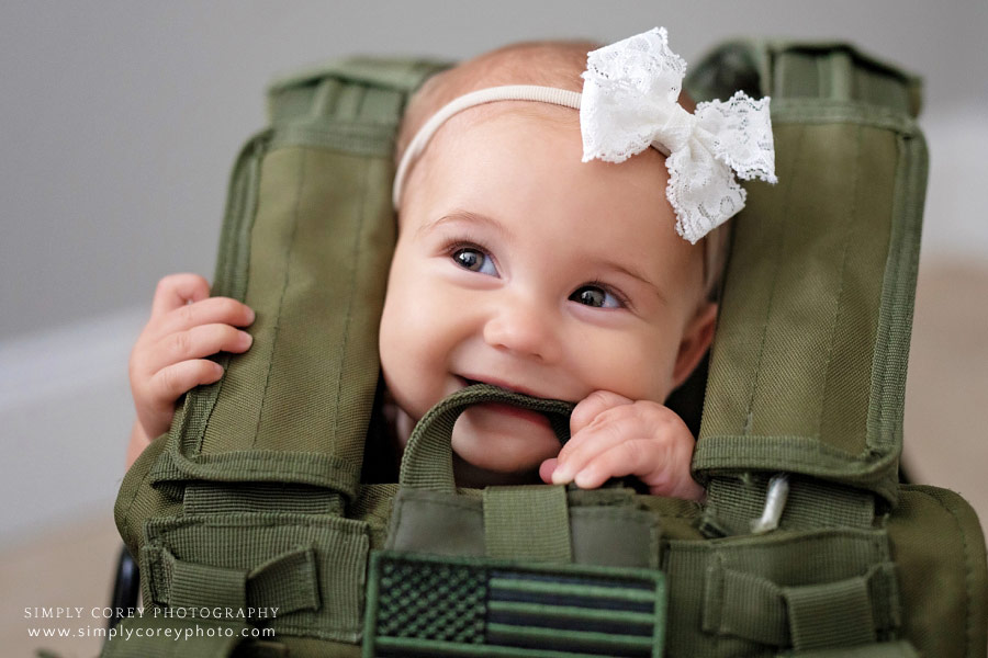Peachtree City baby photographer, girl with bow smiling in dad's tactical vest