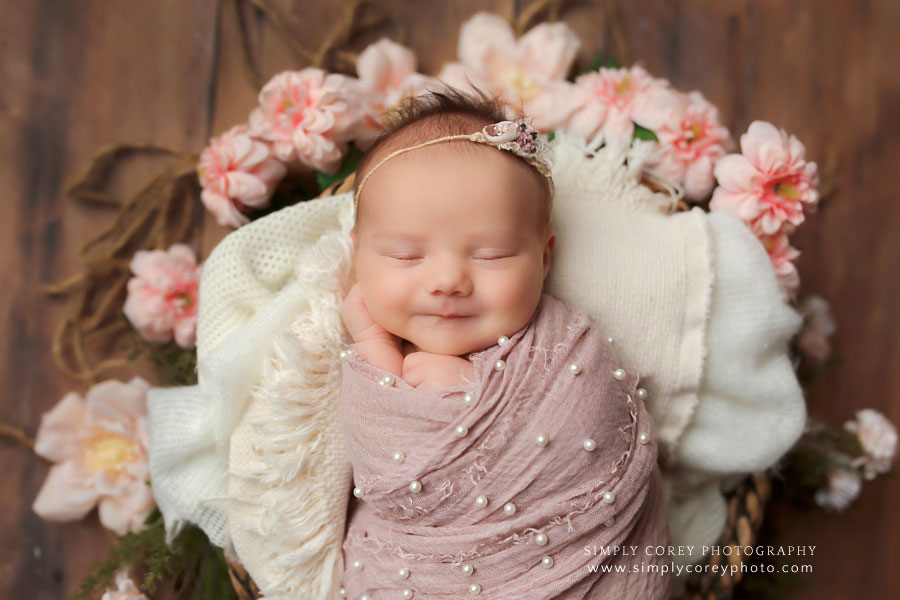 newborn photographer near Newnan, smiling baby girl in basket with pink pearl wrap and flowers