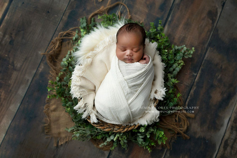 newborn photographer near Newnan, baby boy in basket with white wrap and greenery