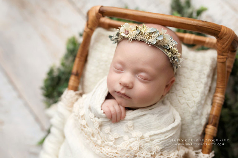 Newnan newborn photographer, baby girl in rattan bed with flower crown and greenery