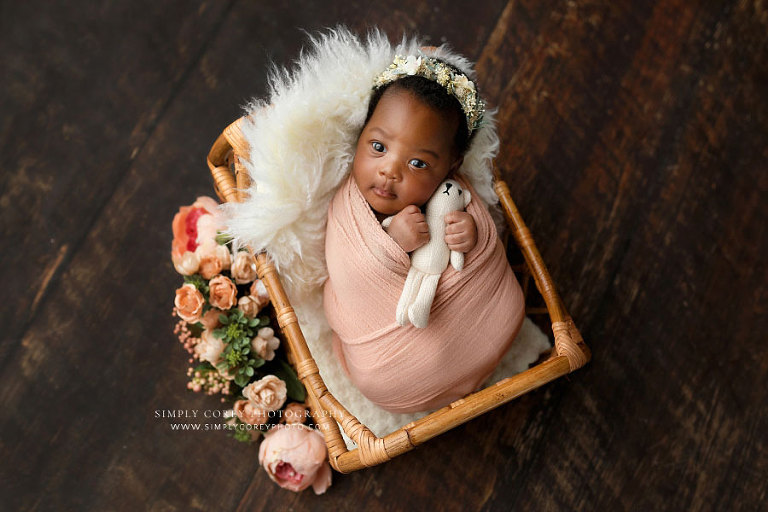 newborn photographer near Carrollton, GA; baby girl in pink wrap with teddy bear and flowers