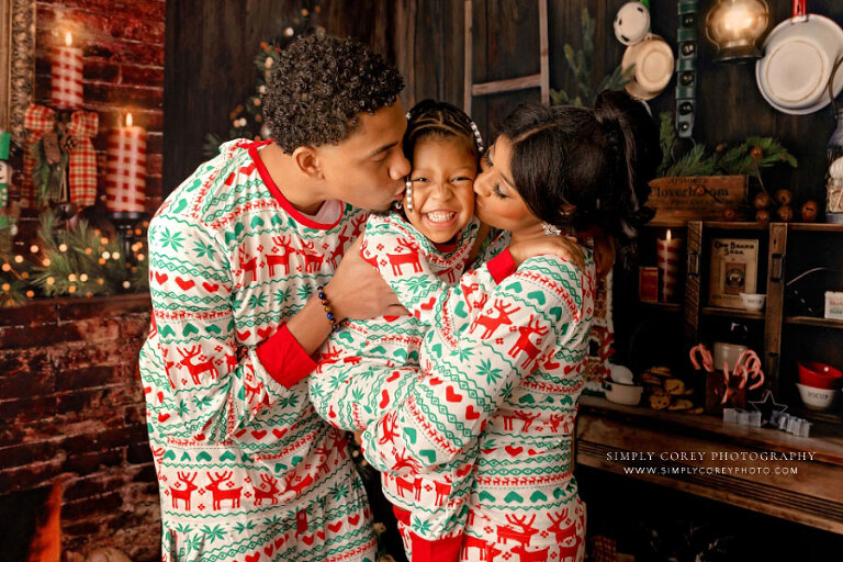 Villa Rica Christmas mini session photographer, parents kissing child in holiday pajamas