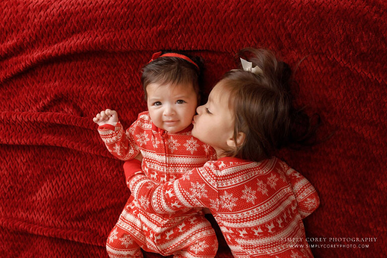 West Georgia mini session photographer, big sister in Christmas pajamas kissing baby sister