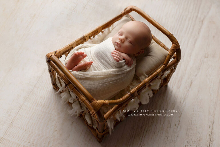 newborn photographer near Carrollton, GA; swaddled baby boy in rattan bed