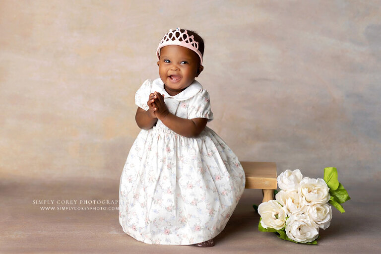 baby photographer near Carrollton, GA; girl clapping and smiling on studio backdrop