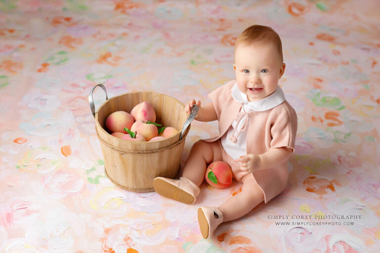 Atlanta baby photographer, smiling girl with basket of peaches on floral backdrop