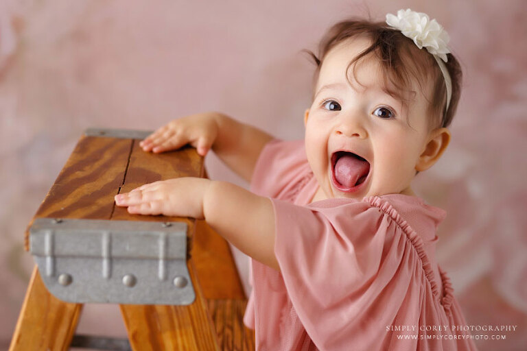 baby photographer near Atlanta, girl in pink laughing while holding ladder