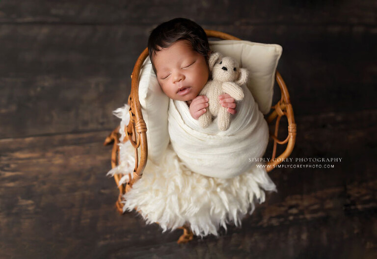 newborn photographer near Atlanta, baby boy in studio with rattan chair and ivory swaddle and bear