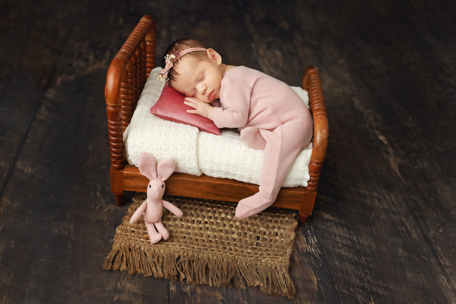 newborn photographer near Tyrone baby girl in pink pajamas on bed prop