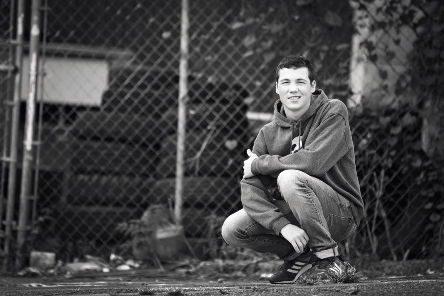 senior portrait photographer near Villa Rica, teen by fence and tires