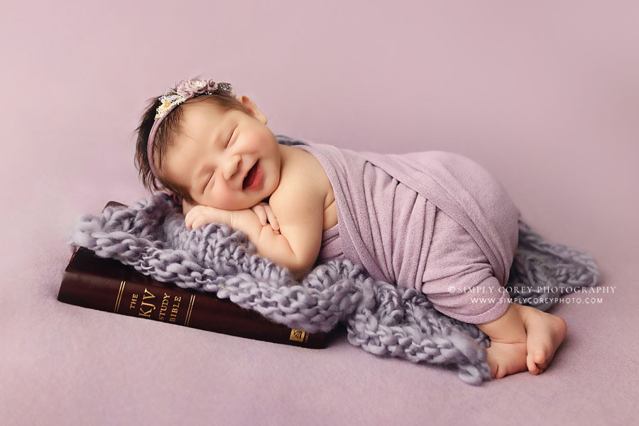newborn photographer near Newnan, baby in purple smiling with Bible in studio
